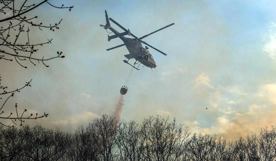 In this photo taken Monday, May 4, 2015, a helicopter dumps water on a brush fire behind houses along Cragsmoor Rd. in Cragsmoor, N.Y. The fire, which started just before noon on Sunday in the Town of Mamakating, has affected more than 1,700 acres of the Shawangunk Ridge State Forest. (Allyse Pulliam/Times Herald-Record via AP)