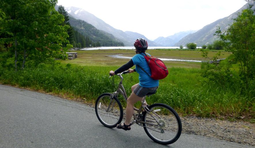 ADVANCE FOR WEEKEND EDITIONS, MAY 9-10 - In this photo taken May 26, 2014, Deb Hansen pedals a rental bike along the road out of Stehekin, Wash., after backpacking the Lake Chelan Lakeshore Trail. Stehekin is a Northwest classic backcountry destination at the end of Lake Chelan, accessible by boat and floatplane and, most deliciously, by foot. (Rich Landers/The Spokesman Review via AP)