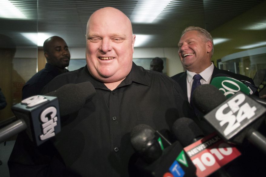 FILE - In this Nov. 21, 2014, file photo, Toronto's outgoing Mayor Rob Ford, front center, stands next to his brother Doug Ford outside his office as he speaks with the media before signing bobblehead dolls in his likeness in Toronto. Doctors have removed a cancerous tumor from the former Toronto mayor's abdomen and he has regained consciousness after an intensive surgery that kept him under anesthesia for about 10 hours, his chief of staff said late Monday, May 11, 2015. (AP Photo/The Canadian Press, Chris Young, File)