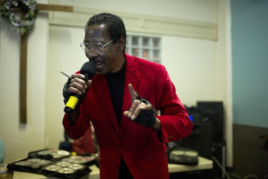 In this Wednesday, Feb. 4, 2015 photo, sporting a red velvet jacket, 63-year-old Skid Row resident Vincent Washington sings a song at karaoke night at the Central City Community Church of the Nazarene on Skid Row in Los Angeles. As people harmonize on Beatles songs, they begin to lock out the ugliness outside, where a misdirected look can launch a knife fight in a second. Where across 50 square blocks on the edge of City Hall and other landmarks that represent the rich and powerful the streets reek with the smell of urine. Where some 1,700 people bed down on filthy sidewalks every night. (AP Photo/Jae C. Hong)