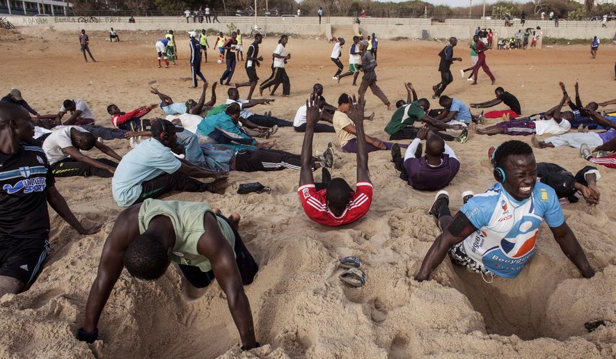In this photo taken on Tuesday, May 7, 2015, people take part in different type of sport moves, including push ups over dug out holes in the sand at Fann Beach in Dakar, Senegal. It isn’t Venice Beach, it’s Fann Beach, and the sounds of waves serves as a background rhythm for hundreds of super-fit, sport loving Senegalese who swarm to the beach en masse every day for a workout to chants and cheers. (AP Photo/Jane Hahn)