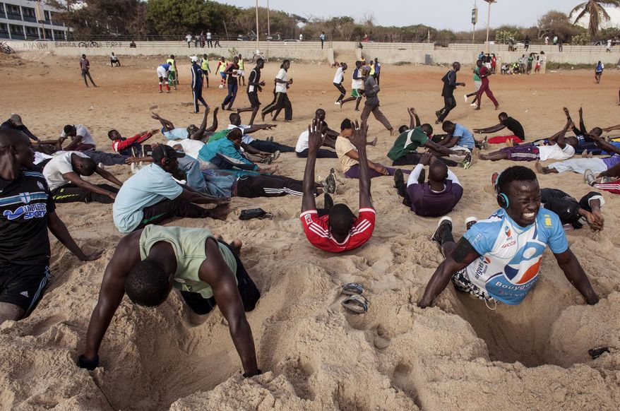 In this photo taken on Tuesday, May 7, 2015, people take part in different type of sport moves, including push ups over dug out holes in the sand at Fann Beach in Dakar, Senegal. It isn’t Venice Beach, it’s Fann Beach, and the sounds of waves serves as a background rhythm for hundreds of super-fit, sport loving Senegalese who swarm to the beach en masse every day for a workout to chants and cheers. (AP Photo/Jane Hahn)