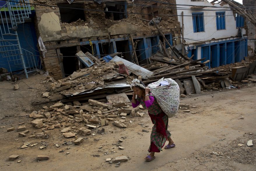 A Nepalese woman carrying belongings walks past a damaged house in Chautara, Nepal, Wednesday, May 13, 2015. The condition of many of the buildings damaged in the April 25 earthquake, got worse after the magnitude-7.3 quake Tuesday. (AP Photo/Bernat Amangue)