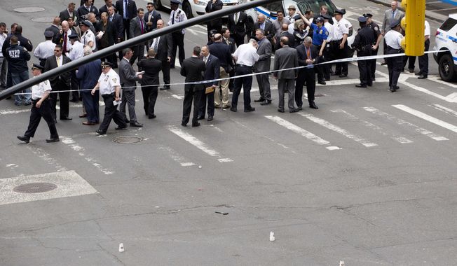 A hammer, bottom center between three white cups, lies in the middle of a Manhattan intersection as police investigators gather, Wednesday, May 13, 2015, after a man apparently wielding the hammer was shot and wounded by police in New York. The shooting took place shortly after 10 a.m. Wednesday blocks from Madison Square Garden and Penn Station in Manhattan. (AP Photo/Mark Lennihan)