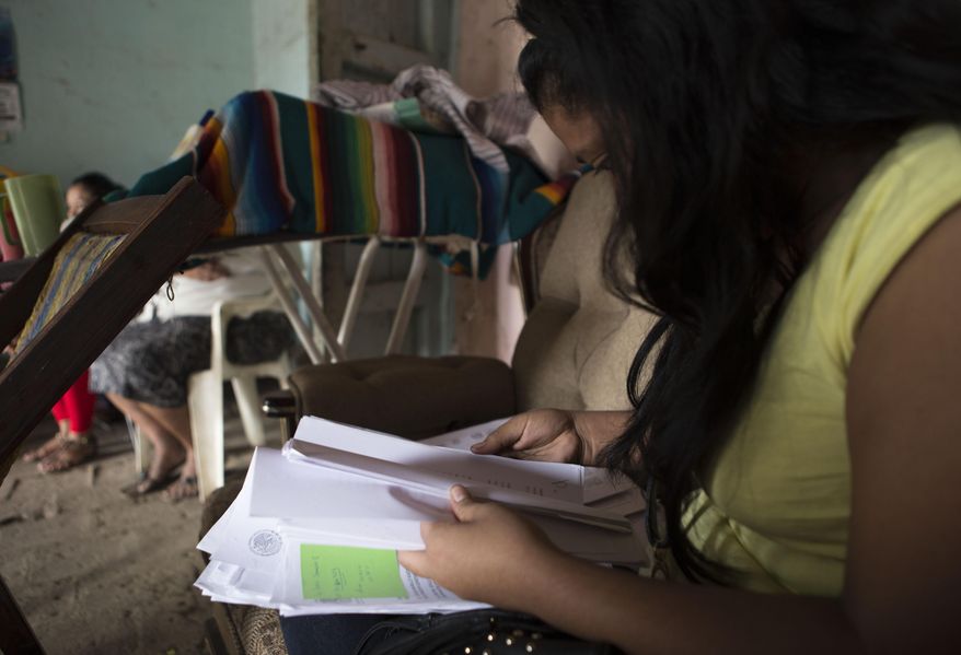 FILE - In this Dec. 23, 2014 file photo, a woman who spoke on the condition of anonymity in fear retribution by officials and drug traffickers, looks through court documents at her home in Arcelia, Mexico, during her first interview since being tortured and falsely imprisoned for five months on weapons possession charges. The Mexican government said Thursday, May 14, 2015 it will give at least 50 million pesos ($3.3. million) to the relatives of criminal suspects slain in 2014 by soldiers and survivors of the shootings, after a rights investigation found 12 to 15 of the 22 suspects were killed by army troops after surrendering. The investigation found the victims included three women who survived the attack and were tortured or pressured to support the army's version that all 22 suspects were killed in a shootout. (AP Photo/Christian Palma, File)