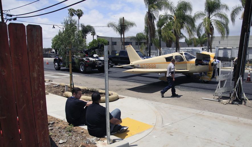 The pilot and passenger watch from the sidewalk as their small aircraft prepares to be towed, Saturday, May 16, 2015 in Santee, Calif. The pilot had to make an emergency landing near Cuyamaca Street and Prospect Avenue in Santee Saturday. No injuries were reported. (Misael Virgen/U-T San Diego via AP) NO SALES; COMMERCIAL INTERNET OUT; MANDATORY CREDIT