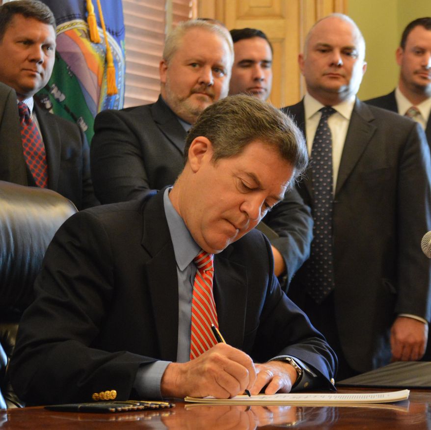 Kansas Gov. Sam Brownback signs legislation overhauling how the state collects taxes from businesses to finance benefits for unemployed workers, Monday, May 18, 2015, at the Statehouse in Topeka, Kan. The new law is designed to make businesses' taxes more predictable and sets a new maximum cap on weekly benefits. (AP Photo/Nicholas Clayton)