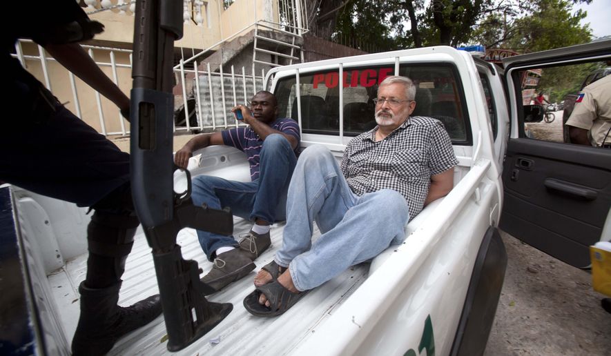 FILE - In this Friday, Sept. 5, 2014, file photo, U.S. citizen Michael Karl Geilenfeld waits in handcuffs as the manager of his orphanage sits with him in the back of a police truck outside the St. Joseph's Home For Boys after police closed it down in the Delmas area of Port-au-Prince, Haiti. Haitian justice authorities said Monday, May 18, 2015, that they are making plans for a new criminal trial against Geilenfeld who has been accused of physically and sexually abusing boys in an orphanage that he has run for decades in the impoverished Caribbean country. (AP Photo/Dieu Nalio Chery, File)