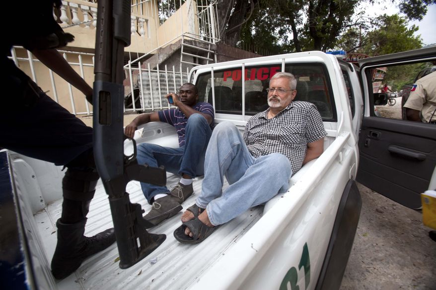 FILE - In this Friday, Sept. 5, 2014, file photo, U.S. citizen Michael Karl Geilenfeld waits in handcuffs as the manager of his orphanage sits with him in the back of a police truck outside the St. Joseph's Home For Boys after police closed it down in the Delmas area of Port-au-Prince, Haiti. Haitian justice authorities said Monday, May 18, 2015, that they are making plans for a new criminal trial against Geilenfeld who has been accused of physically and sexually abusing boys in an orphanage that he has run for decades in the impoverished Caribbean country. (AP Photo/Dieu Nalio Chery, File)