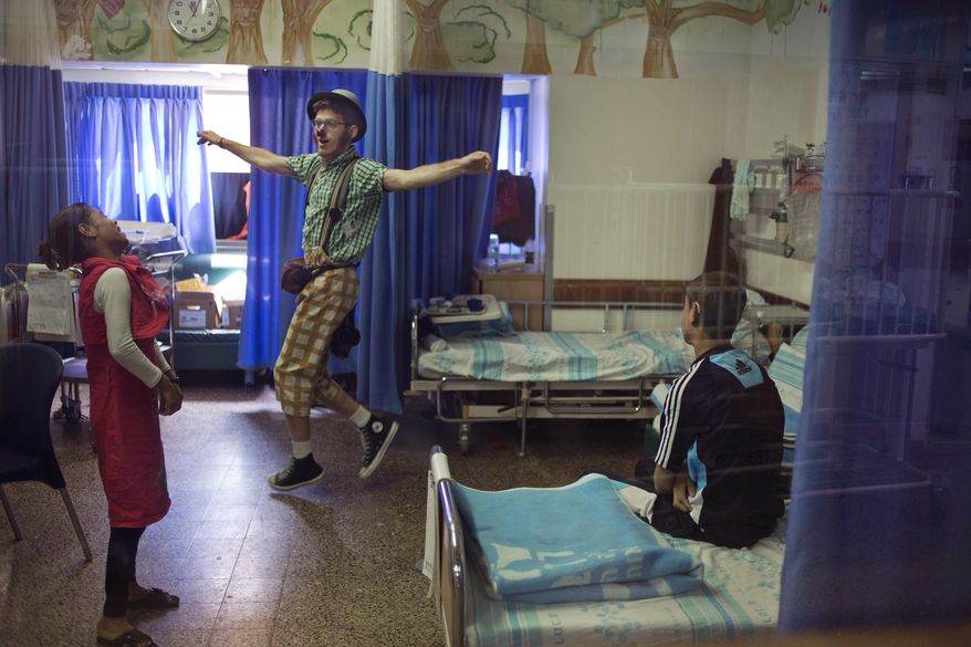 In this Wednesday, May 13, 2015 photo, Palestinian siblings Ahmed, right, and Hadeel Hamdan watch medical clown who goes by the name 'Juhl' perform, at the Rambam Health Care Campus in Haifa, Israel. The bedroom of Palestinian Ahmed and Hadeel looks like a hospital ward, filled with beeping machines, monitors, solution bags and sterilizing fluids. This is where the Gaza teenagers spend 12 hours a day connected to dialysis machines. These contraptions and their hopes for a better life come from a surprising source: an Israeli hospital. (AP Photo/Ariel Schalit)