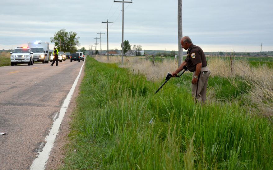 In this photo taken Monday, May 18, 2015, a Weld County Sheriff’s Office deputy uses a metal detector to sweep for evidence in Windsor, Colo., after a cyclist was fatally shot. Lt. Richard Higuera says 48-year-old John Jacoby was cycling northwest of Windsor Lake when he was shot Monday morning. A passing motorist found his body. (Jason Pohl/The Coloradoan via AP) MANDATORY CREDIT