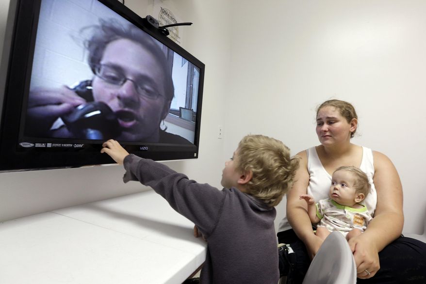 In this photo taken on Tuesday, May 5, 2015, inmate Jesse Cole is shown on a television screen as his son William, 4, center, reaches to touch the screen while his mother, Edna, holds 8-month-old Jesse James, during a video visitation with at the Fort Bend County Jail, in Richmond, Texas. Prisoners’ rights advocates are worried that the growing use in the U.S. of video technology to facilitate visits between inmates and their family and friends at county jails and prisons is part of a trend to eliminate the more traditional in-person visit. But officials who run these facilities say video visitation has been a boon to their efforts to improve security and increase visiting hours. (AP Photo/David J. Phillip)