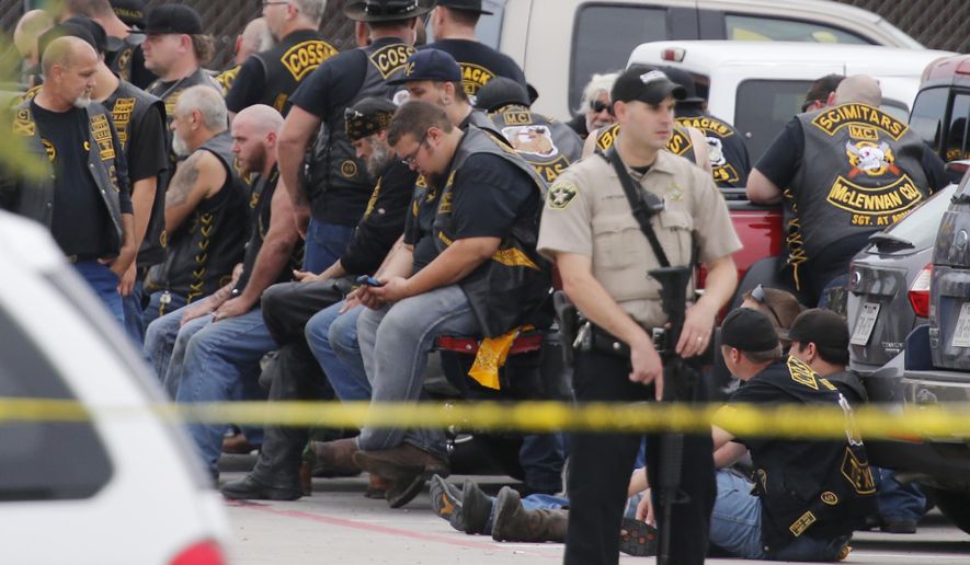 FILE - In this May 17, 2015 file photo, a McLennan County deputy stands guard near a group of bikers in the parking lot of a Twin Peaks restaurant in Waco, Texas. The prevailing images of protests in Baltimore and Ferguson, Missouri, over police killings of black men were of police in riot gear, handcuffed protesters, tear gas and mass arrests. The main images of a fatal gun battle between armed bikers and police in Waco, Texas, also showed mass arrests _ carried out by nonchalant-looking officers sitting around calm bikers on cell phones. (Rod Aydelotte/Waco Tribune-Herald via AP)