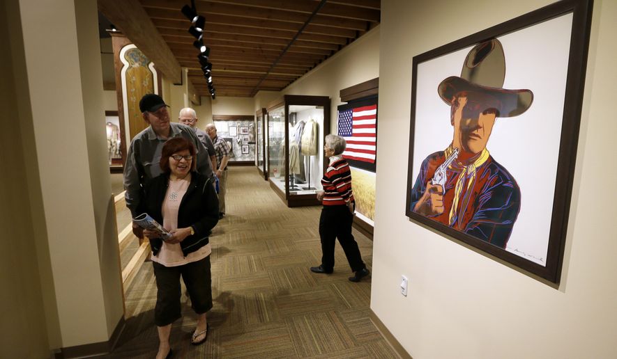 Tourists walk past an Andy Warhol print of John Wayne on display in the John Wayne Museum, Thursday, May 14, 2015, in Winterset, Iowa. Though Wayne moved to California at a young age, it’s a minor footnote for Winterset, a city of about 5,000 people. On Saturday, May 23, 2015, Winterset will help launch the official opening of the newly built museum celebrating Wayne’s life and career. (AP Photo/Charlie Neibergall)