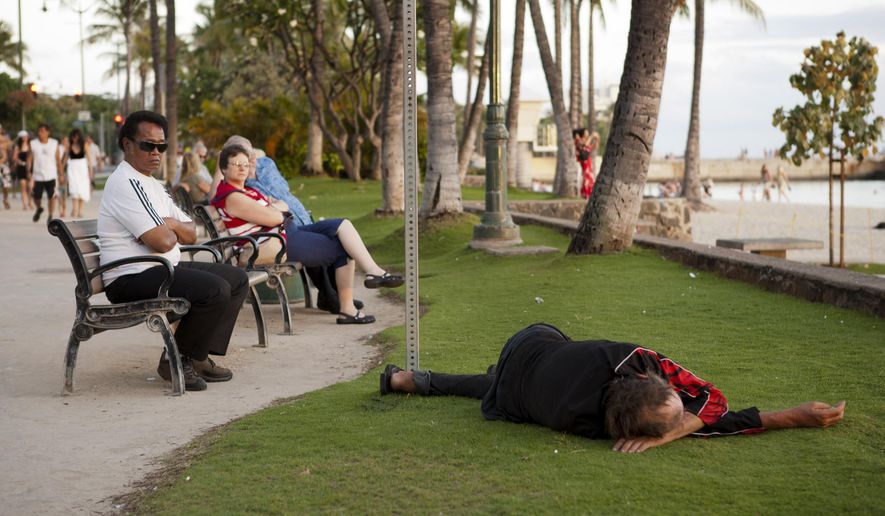FILE - In this May 13, 2011, file photo, tourists watch the sunset as a man sleeps on the grass near Waikiki Beach in Honolulu. Honolulu Mayor Kirk Caldwell has vetoed a bill that would have expanded the city's ban on sitting and lying down on sidewalks. Caldwell said Thursday, May 21, 2015, that the city would face legal challenges if he signed Bill 6 into law. His administration is proposing an alternative that he says the city can defend. (AP Photo/Marco Garcia, File)