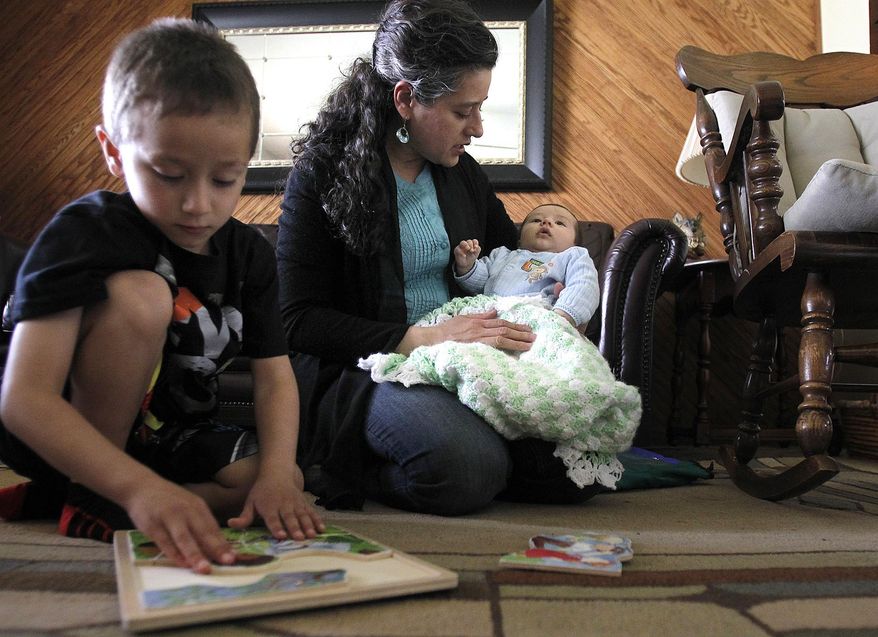 In this April 13, 2015 photo, Elizabeth Rios tends to her 8-week-old son Emmanuel while helping her son Daniel, 4, with puzzles at her home in Crystal Lake, Ill. Rios is on maternity leave from her job as a nurse practitioner at the Harvard Area Community Health Center and has recently been featured in Migrant Clinician Network’s 30 Clinicians Making A Difference. Rios, 39, has spent the past four years making similar connections with migrant and seasonal workers in McHenry County. It’s a dream job, she said, because she serves a population that might otherwise go unheard or misunderstood. (Matthew Apgar/Northwest Herald via AP) CHICAGO OUT MANDATORY CREDIT