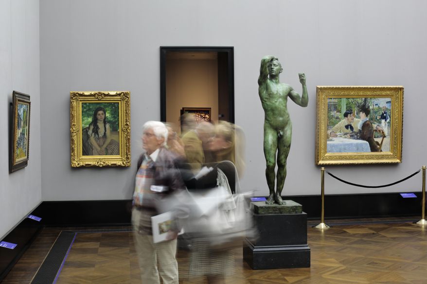 In this photo taken with a long shutter, members of the media walks through the exhibition 'Impressionism - Expressionism. Turning Point in Art' during the press preview at the Alte Nationalgalerie (Old National Gallery), in Berlin, Germany, Wednesday, May 20, 2015. The paintings from left: Le Pont de Chatou by Maurice de Vlaminck, L'Ete by Auguste Renoir, the sculpture L'Age d'airain by Auguste Renoir and the painting Chez le pere Lathuille by Edouard Manet. The exhibition opens on May 22, and runs through Sept. 20, 2015. (AP Photo/Markus Schreiber)