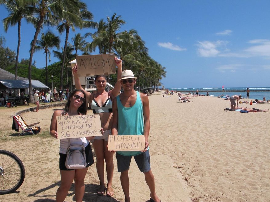 Pohai George, left, Ashley Montogmery and Nathaniel Whittaker, right, protested against Monsanto at a Waikiki Beach rally in Honolulu on Saturday, May 23, 2015. They were part of an international day of protests against the company. (AP Photo/Cathy Bussewitz)