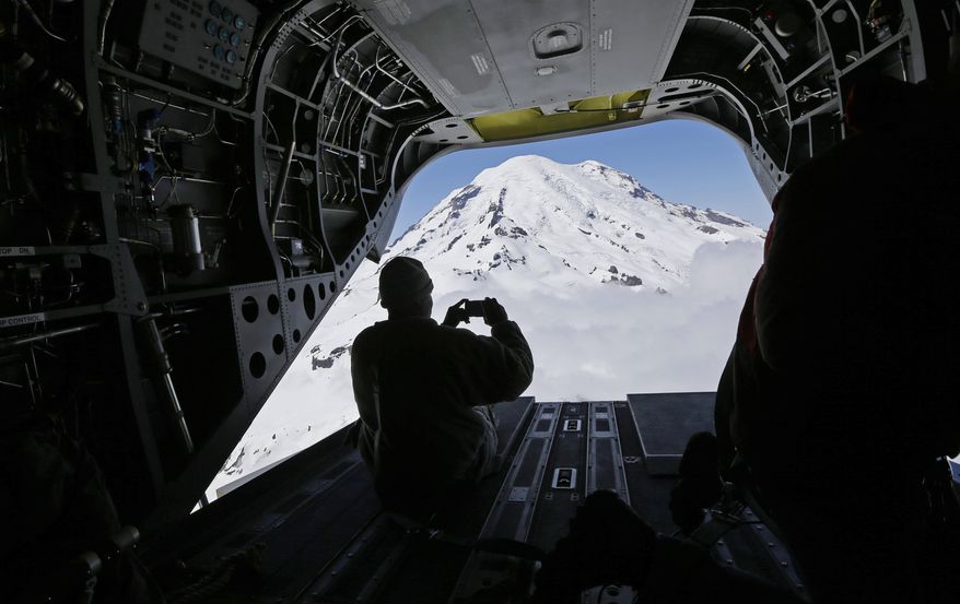 In this photo taken May 15, 2015, U.S. Army Reserve Sgt. Charlesell Thrower takes a photo of Mount Rainier out the open rear door of a Boeing CH-47F Chinook helicopter as it flies in Washington state to give members of the media a view of mountain search and rescue training exercises involving another CH-47F. (AP Photo/Ted S. Warren)