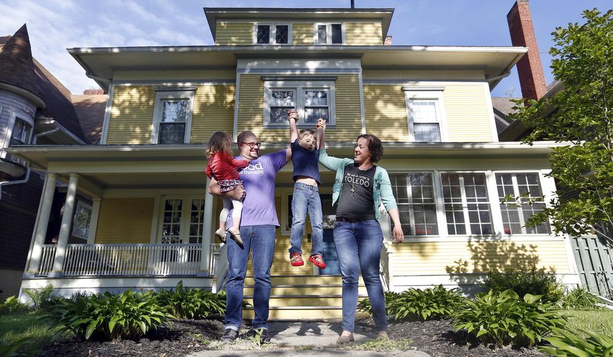 In this May 14, 2015 photo, Jamie, second left, and Kelly Rye, right, pose for photos with their children Jane, 2, left, and Jonah, 5, in front of their 3,400-square-foot home in Toledo, Ohio. The Ryes will soon move out of their 3,400-square-foot home, which sold after only a little advertising on a private neighborhood Facebook page, and into a 400-square-foot "tiny house." (Amy E. Voigt/The Blade via AP) MANDATORY CREDIT; MAGS OUT; NO SALES; TV OUT; SENTINEL-TRIBUNE OUT; MONROE EVENING NEWS OUT; TOLEDO FREE PRESS OUT
