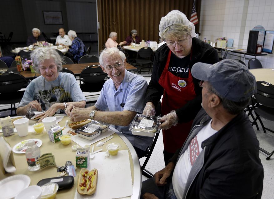 In this Thursday, May 7, 2015 photo, volunteer Sandy Lockhart, standing, serves lunch to John Pearson, right, as Dorothy Christian, left, and her husband, Fredrick, look on at a seniors meal program at the Rush Park Community Center in Citrus Heights, Calif. The program, run by the Meals on Wheels by ACC, provides free meals to senior citizens at the center and brings them meals at their homes. Meals on Wheels is among the programs that have received funds from the state Assembly's own administrative budget for programs that faced cuts in state and other funding. (AP Photo/Rich Pedroncelli)