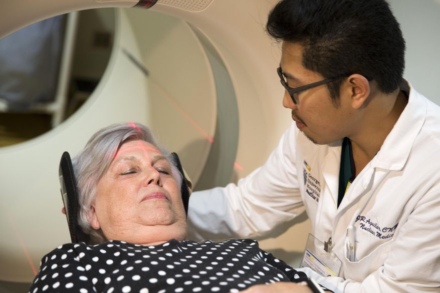 In this photo taken May 19, 2015, Judith Chase Gilbert, of Arlington, Va., is loaded into a PET scanner by Nuclear Medicine Technologist J.R. Aguilar at Georgetown University Hospital in Washington. Gilbert shows no signs of memory problems but volunteered for a new kind of scan as part of a study peeking into healthy brains to check for clues about Alzheimer's disease. (AP Photo/Evan Vucci)