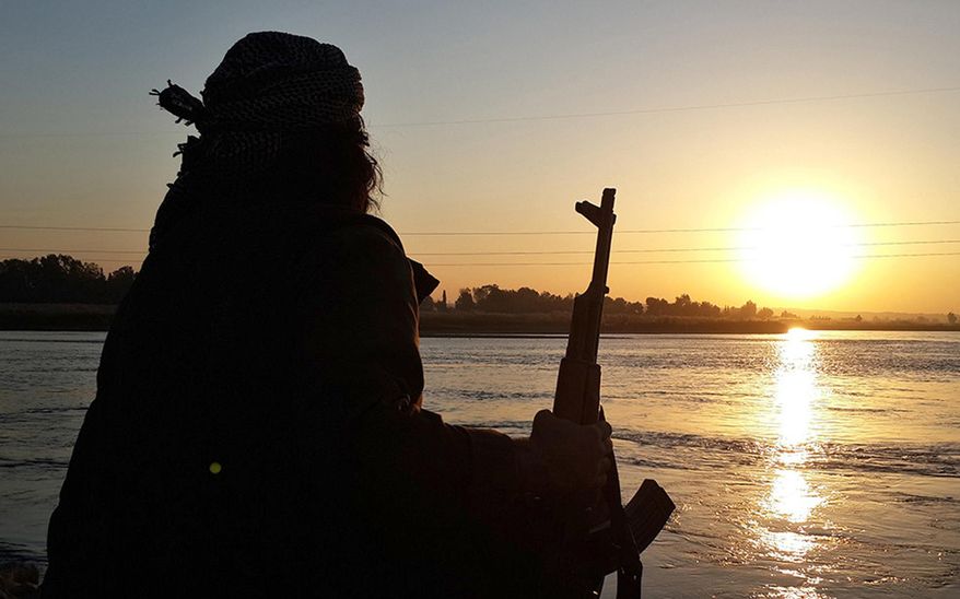 In this photo released on Sept. 29, 2014 by a militant website, which has been verified and is consistent with other AP reporting, an Islamic State group fighter holds his AK-47 machine gun as he relaxes on the bank of the Euphrates river in Raqqa, Syria. The IS group has set up a generous welfare system to help settle and create lives for the thousands of jihadis, men and women, who have flocked to IS territory from the Arab world, Europe, Central Asia and the United States. (Militant website via AP)