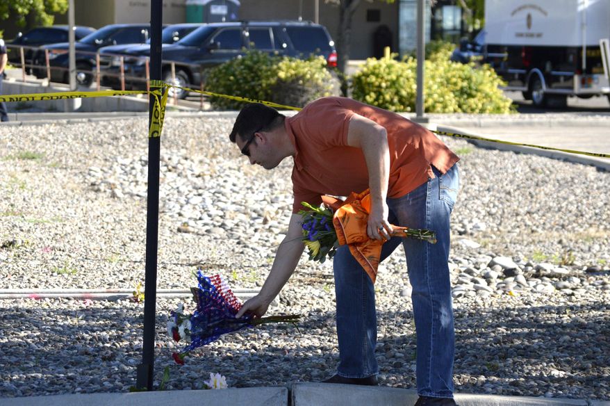 A man leaves flowers on Tuesday, May 26, 2015 near the site where authorities say a Rio Rancho police officer was shot late Monday during a traffic stop in the Albuquerque, New Mexico, suburb. Police say the officer later died at a hospital. A person believed to be involved in the shooting was taken into custody in the Albuquerque area but authorities are still searching for another suspect. (AP Photo/Russell Contreras)