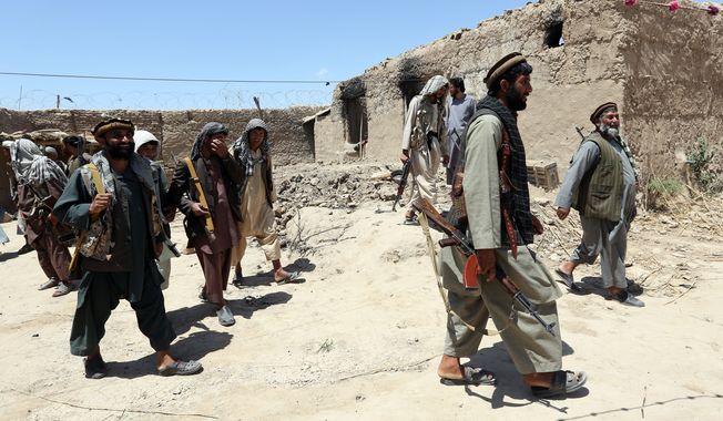 In this Thursday, May 21, 2015 photo, local militia group fighters walk past a building torched by Taliban fighters at Talawka village in Kunduz province, north of Kabul, Afghanistan. Fighting has been raging in Kunduz for more than a month. Pushed back by army reinforcements that arrived days after the assault began, insurgents now occupy villages in Gor Tepa, 15 kilometers (12 miles) from the provincial capital, also called Kunduz. (AP Photo/Rahmat Gul)