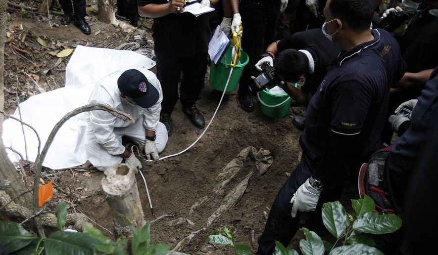 Malaysian police forensic team members inspect a freshly exhumed human body from an unmarked grave in Wang Burma at the Malaysia-Thailand border outside Wang Kelian, Malaysia Tuesday, May 26, 2015. Malaysian authorities have found one corpse as they started digging for bodies at an abandoned jungle camp used by human traffickers on the border with Thailand. The discovery came as forensics teams began the grim task of exhuming nearly 140 suspected graves in the mountainous area where trafficking syndicates were known to hold migrants for ransom. (AP Photo/Joshua Paul)