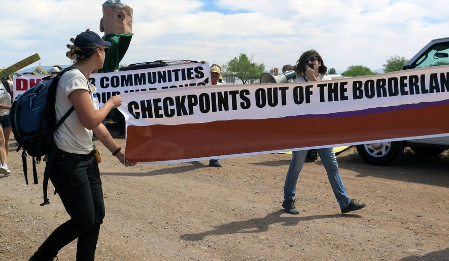 Two protesters carry a large banner as they walk toward a U.S. Border Patrol checkpoint on a two-lane road in Amado, Ariz. on Wednesday, May 27, 2015, about 20 miles north of the border with Mexico. The protesters come from Tucson and from Arivaca, a small community whose residents must drive through the checkpoint to leave town. They say the checkpoint is a nuisance and leads to racial profiling. (AP Photo/Astrid Galván)