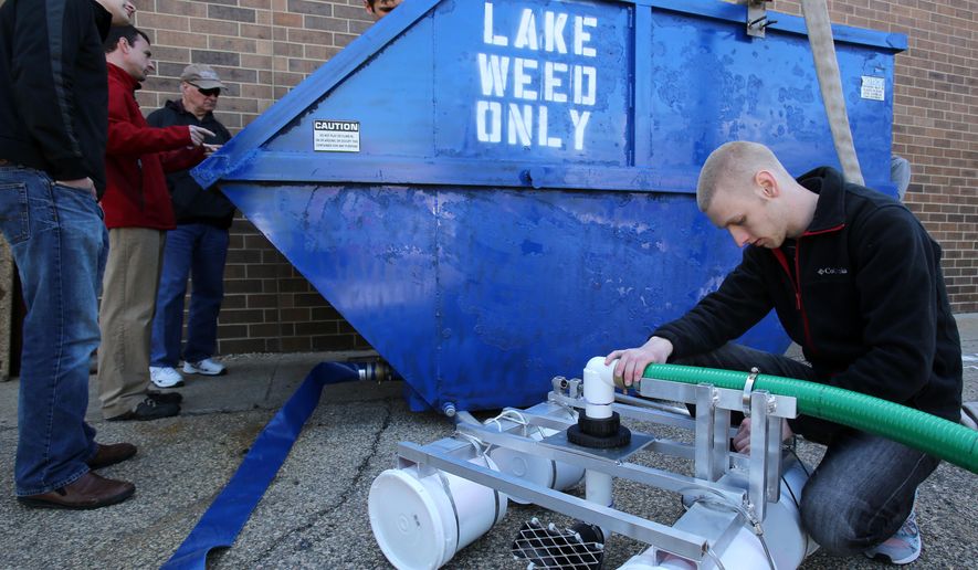In this photo taken Thursday, May 21, 2015, Madison Area Technical College introduction to engineering student Tyler Lecy, right, checks the pipe clamps on an intake device that is part of a machine created to remove algae from the local lakes, outside the school in Madison, Wis. (Amber Arnold/Wisconsin State Journal via AP)