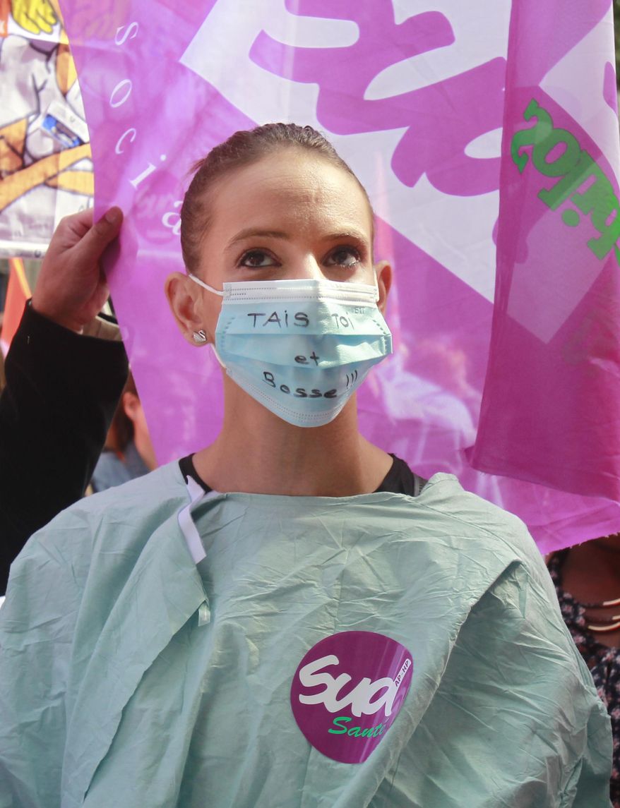 A nurse wearing a surgical mask with the slogan 'Shut up and Work' demonstrates in Paris, France, Thursday May 28, 2015, outside the headquarters of Paris’ regional hospital authority. Thousands of doctors, nurses and other hospital personnel are demonstrating in central Paris to protest a planned working-hours reform they say will result in more burnout and worse patient care. Banners with slogans like “Taking away our rights never made the economy grow” lined the roadway near the city’s Renaissance-style city hall, visible in background. (AP Photo/Remy de la Mauviniere)