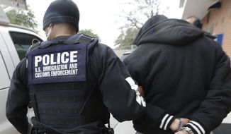 A U.S. Immigration and Customs Enforcement agent escorts a handcuffed illegal immigrant convicted of a felony that was taken into custody during an early morning operation in Dallas on March 6, 2015. (Associated Press) ** FILE **