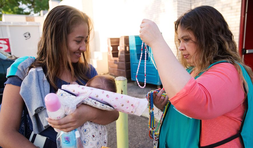In this April 30, 2105 photo, Mayra Garza, the floor manager at a Catholic Charities respite center, hands a rosary to 24-year-old Jeysel Leyba Amaya before Amaya gets on a bus headed to the downtown station in McAllen, Texas. Amaya fled El Salvador with her four-month-old daughter and her sister who received unwanted advances from a gang member there. Rather than getting locked up in a family detention facility, some families, like Amaya, are released by Border Patrol with notices to appear in immigration court. (AP Photo/Seth Robbins)