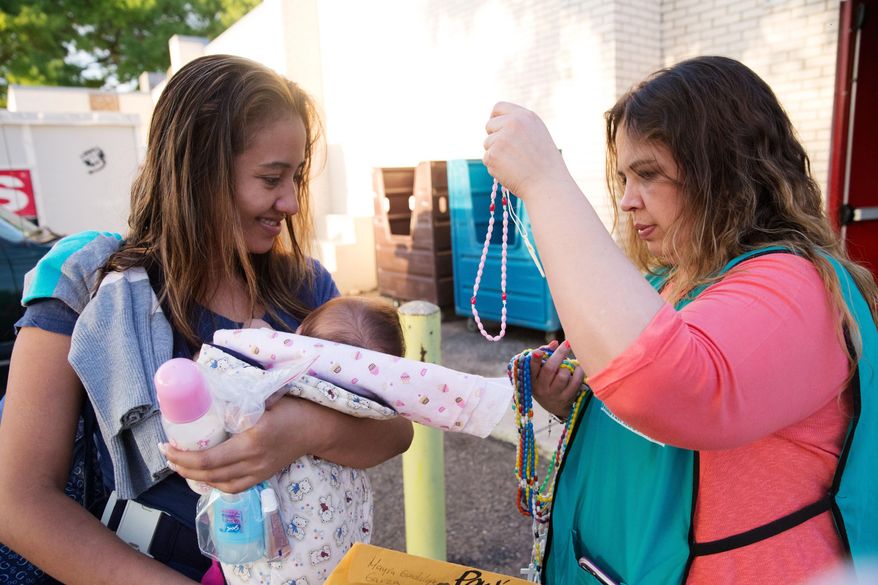 In this April 30, 2105 photo, Mayra Garza, the floor manager at a Catholic Charities respite center, hands a rosary to 24-year-old Jeysel Leyba Amaya before Amaya gets on a bus headed to the downtown station in McAllen, Texas. Amaya fled El Salvador with her four-month-old daughter and her sister who received unwanted advances from a gang member there. Rather than getting locked up in a family detention facility, some families, like Amaya, are released by Border Patrol with notices to appear in immigration court. (AP Photo/Seth Robbins)