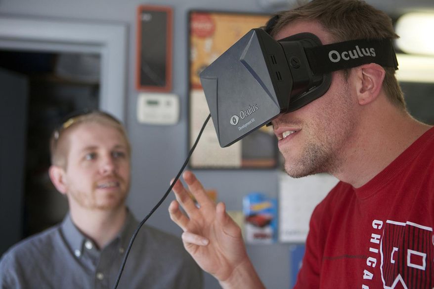 In this April 30, 2015, photo, Matt Groce of Monmouth, Ill., right, uses a pair of Occulus virtual reality goggles to try the video game “Children of Uum” as Rocky Mountain College of Art and Design video game art student and Galesburg native Ricky Davis looks on Thursday at Glory Days Corner Barber Shop In Galesburg, Ill. Davis is a member of 4th Axis Games, the development team for the game, which was previewed at the Denver Comic Con on May 23 through May 25. (Steve Davis/The Register-Mail via AP)