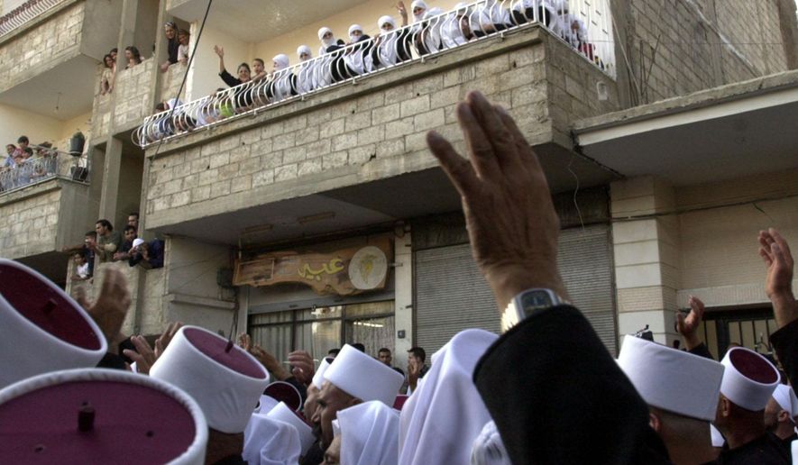 FILE - In this Monday, Sept. 6, 2004 file photo, Druzes in Jaramana, Syria, 45 kilometers (28 miles) west of Damascus, wave from balconies at the nearly 480 Druze clergymen from the Israeli-occupied part of the Golan Heights who crossed into Syria for an annual pilgrimage to a holy shrine in the Syrian countryside. On Thursday, June 11, 2015 an activist group and a Syrian opposition faction said that al-Qaida's affiliate in Syria has killed at least 20 Druze after a confrontation in the northwestern Idlib province, where the jihadi group has forced hundreds of members of the minority sect to covert to Sunni Islam. (AP Photo/Bassem Tellawi, File)