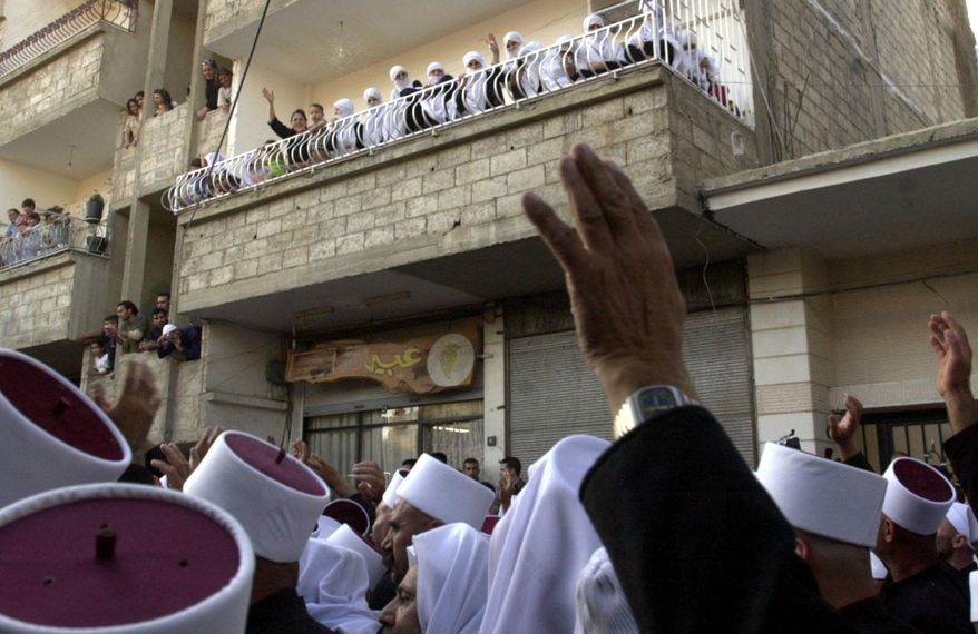 FILE - In this Monday, Sept. 6, 2004 file photo, Druzes in Jaramana, Syria, 45 kilometers (28 miles) west of Damascus, wave from balconies at the nearly 480 Druze clergymen from the Israeli-occupied part of the Golan Heights who crossed into Syria for an annual pilgrimage to a holy shrine in the Syrian countryside. On Thursday, June 11, 2015 an activist group and a Syrian opposition faction said that al-Qaida's affiliate in Syria has killed at least 20 Druze after a confrontation in the northwestern Idlib province, where the jihadi group has forced hundreds of members of the minority sect to covert to Sunni Islam. (AP Photo/Bassem Tellawi, File)