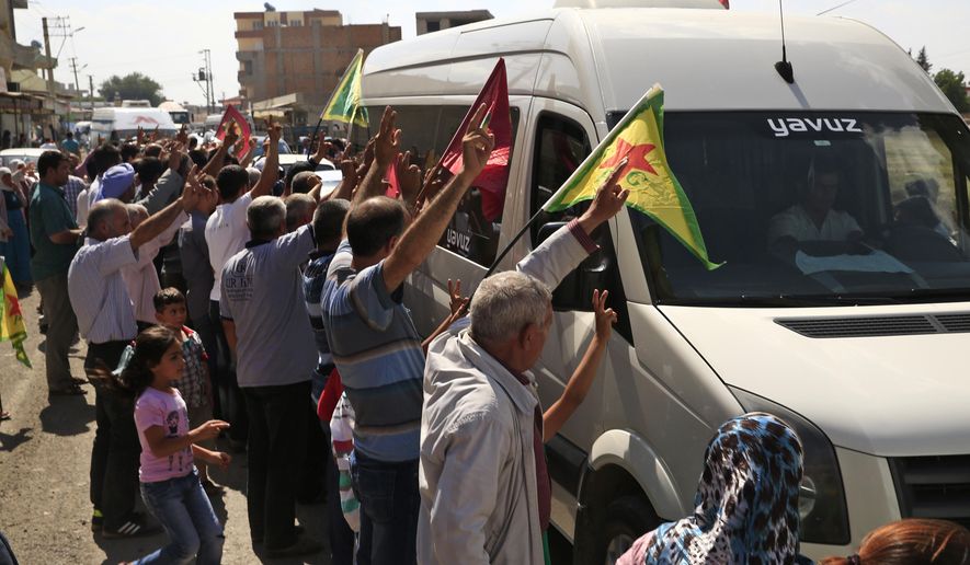 Kurdish people waving flags flash the V-sign and applaud while lining the road, as the convoy carrying the body of U.S. citizen Keith Broomfield, killed in fighting with the militants of the Islamic State group in Kobani, Syria, is driven by through Suruc, on the Turkey-Syria border, Thursday, June 11, 2015. (AP Photo/Lefteris Pitarakis)