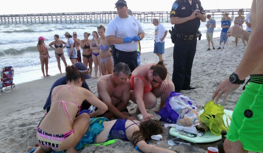 Emergency responders assist a teenage girl at the scene of a shark attack in Oak Island, N.C., Sunday, June 14, 2015. Mayor Betty Wallace of Oak Island, a seaside town bordered to the south by the Atlantic Ocean, said that hours after the teenage girl suffered severe injuries in a shark attack Sunday a teenage boy was also severely injured. (Steve Bouser/The Pilot, Southern Pines, N.C. via AP)