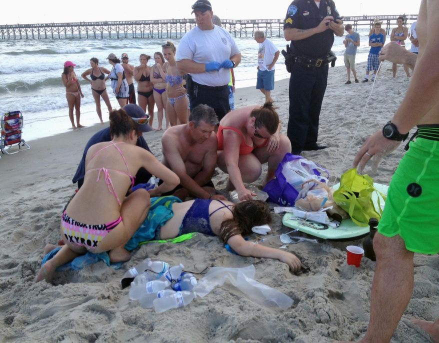 Emergency responders assist a teenage girl at the scene of a shark attack in Oak Island, N.C., Sunday, June 14, 2015. Mayor Betty Wallace of Oak Island, a seaside town bordered to the south by the Atlantic Ocean, said that hours after the teenage girl suffered severe injuries in a shark attack Sunday a teenage boy was also severely injured. (Steve Bouser/The Pilot, Southern Pines, N.C. via AP)