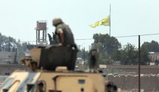 A Turkish soldier on an armored personnel carrier watches as in the background a flag of the Kurdish People&#39;s Protection Units, or YPG, is raised over the city of Tal Abyad, Syria, June 16, 2015. (Associated Press) ** FILE **