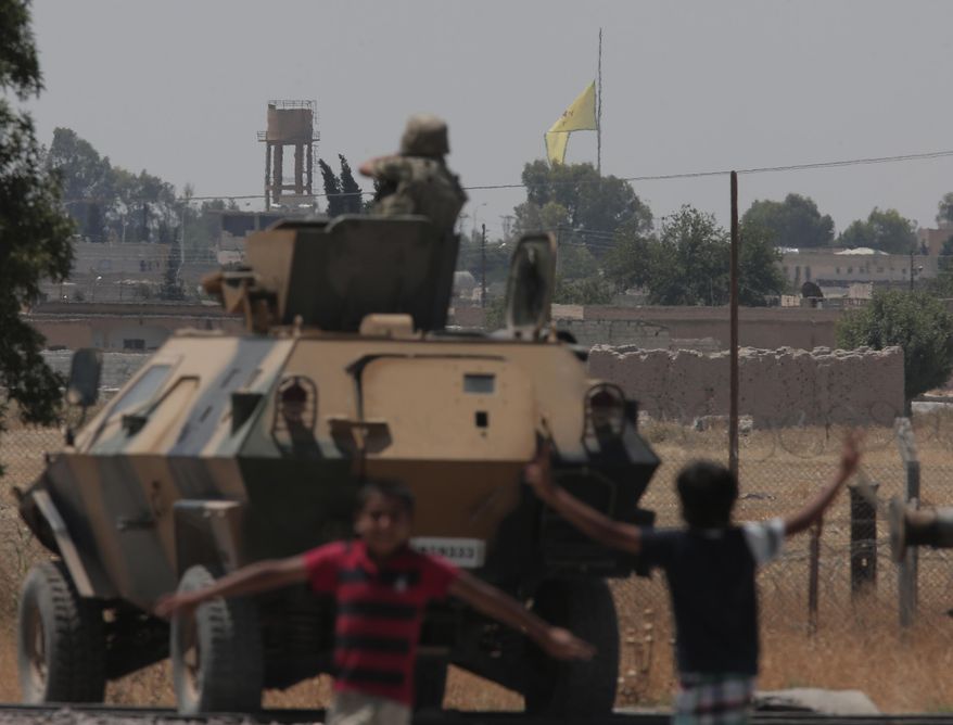 In this photo taken from the Turkish side of the border between Turkey and Syria, in Akcakale, southeastern Turkey, children celebrates as a Turkish soldier on an armoured personnel carrier watches while in the background a flag of the Kurdish People's Protection Units, or YPG, is raised over the city of Tal Abyad, Syria, Tuesday, June 16, 2015. (AP Photo/Lefteris Pitarakis)