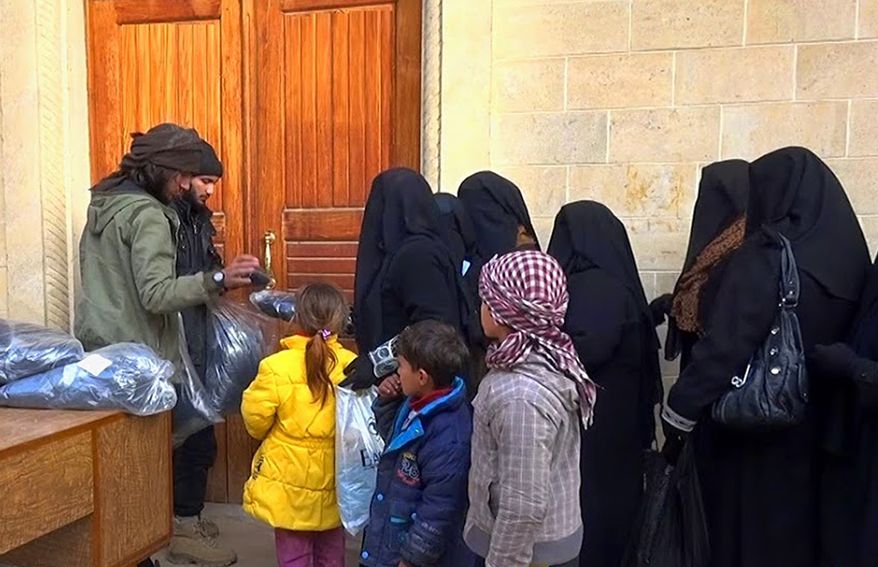 Members of the Islamic State group, left, distribute niqabs, enveloping black robes and veils that leave only the eyes visible, to Iraqi women in Mosul, northern Iraq, June 18, 2015. (Associated Press) ** FILE **