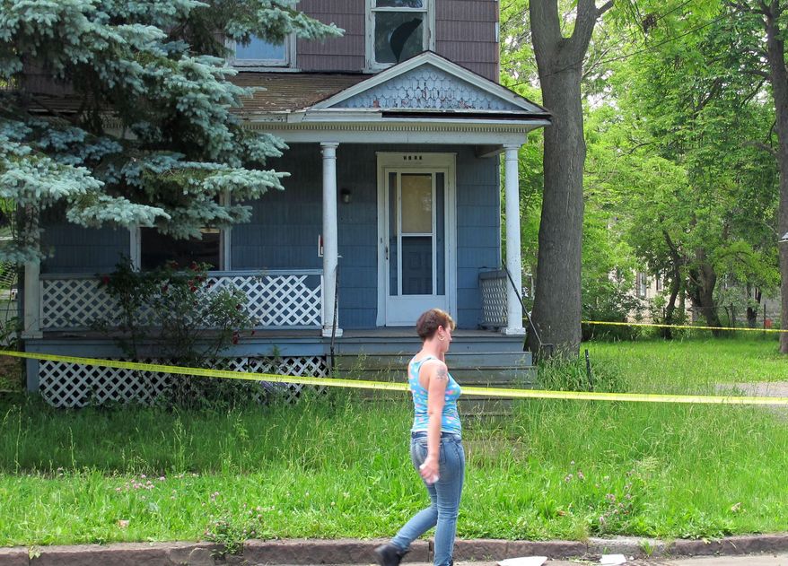 A woman walks by a vacant Niagara Falls, N.Y., house, Thursday, June 18, 2015, two days after the dismembered body of murder victim Terri Lynn Bills was found inside. Another woman was similarly dismembered in Niagara Falls in 2012. That case remains unsolved. (AP Photo/Carolyn Thompson)