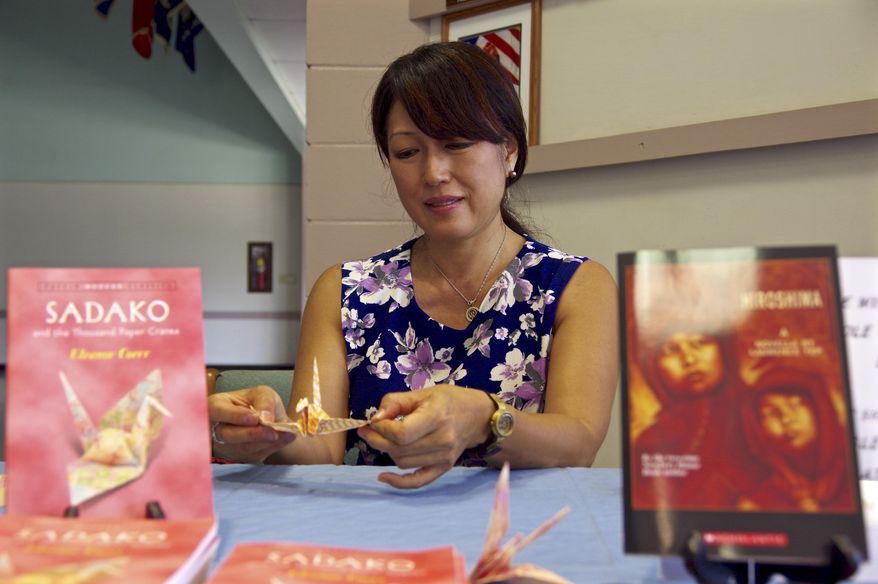 ADVANCE FOR SATURDAY JUNE 20, 2015 AND THEREAFTER- In this Monday, June 15, 2015 photo, Rev. Nicole Sakurai of the Happiness Planting Center is flanked by books on Sadako and Hiroshima as she makes a paper crane during the opening day of the Sadako and Thousand Paper Cranes exhibit at the Kauai Veterans Center in Lihue, Hawaii. The exhibit is an effort to raise peace awareness for the upcoming generations by providing visitors an opportunity to learn more about the effects the atomic bomb has on humanity. (Dennis Fujimoto/The Garden Island via AP)