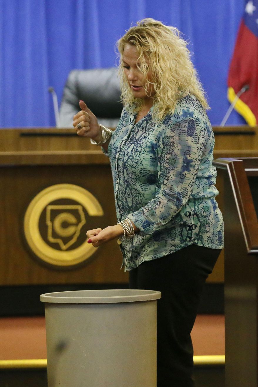 In a Monday, June 22, 2015 photo, Mary Katherine Pursley demonstrates how she says she held a student over a trash can during a hearing before a tribunal at the school system headquarters in Atlanta. Pursley, a Georgia special education teacher who was accused of holding an autistic boy upside-down and lowering him head-first into a trash can while comparing him to Oscar the Grouch says she was trying to calm the boy, not hurt him. (Bob Andres/Atlanta Journal-Constitution via AP) MARIETTA DAILY OUT; GWINNETT DAILY POST OUT; LOCAL TELEVISION OUT; WXIA-TV OUT; WGCL-TV OUT