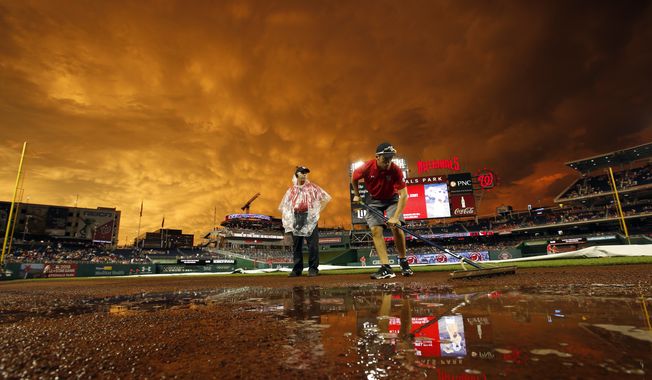A member of the grounds crew works on the field as the sunset turns the sky a golden yellow during a rain delay before a baseball game between the Washington Nationals and the Atlanta Braves at Nationals Park, Tuesday, June 23, 2015, in Washington. (AP Photo/Alex Brandon)