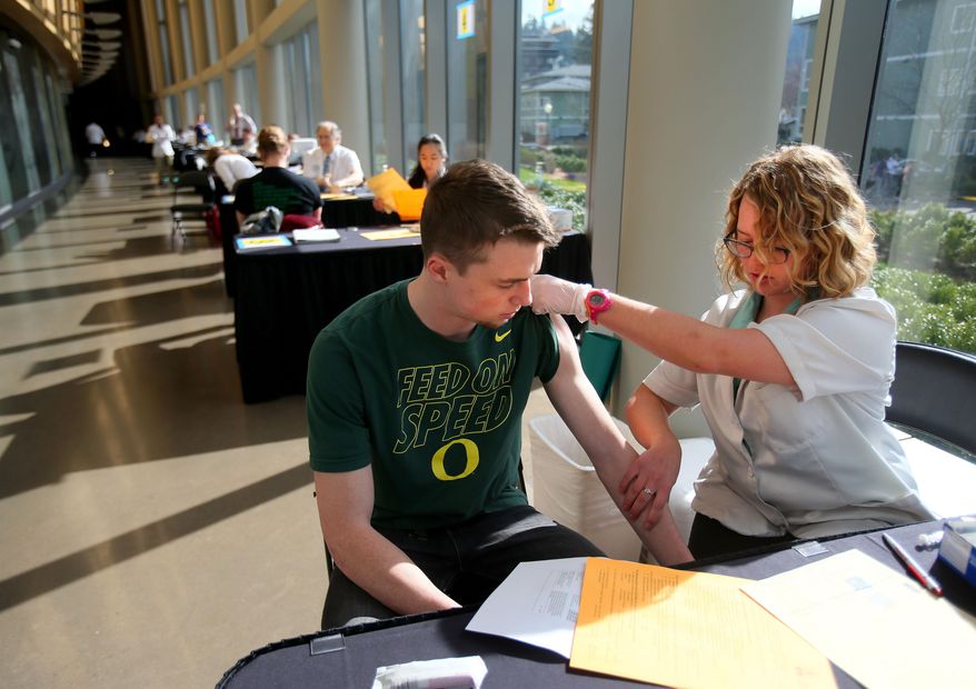 FILE - In this Monday, March 2, 2015 photo, pharmacist Jenna Wright administers the Meningitis B vaccine to University of Oregon freshman Drew Russert during a mass vaccination clinic at Matthew Knight Arena in Eugene, Ore. after an outbreak of meningococcemia, resulting in the death of a student. On Wednesday, June 24, 2015, a federal panel gave a weak endorsement to two new expensive meningitis shots, declining to recommend the vaccines for all teens and leaving the decision to parents and doctors. Students already get another meningitis vaccine that protects against more common strains. (AP Photo/The Register-Guard, Brian Davies)